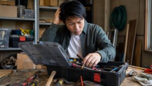 工具箱の中から必要な工具を探す日本人男性と散らかった作業台、工具収納の悩みを表す写真