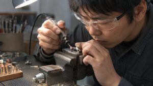 リューターで小さな金属部品の細部を丁寧に研磨する日本人作業者