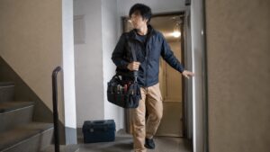 日本人作業員が肩掛け工具バッグを持って通路を移動する様子と床に置かれた工具箱