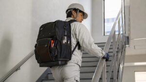 日本人作業員が工具リュックを背負って階段を移動する安全で実用的な作業風景