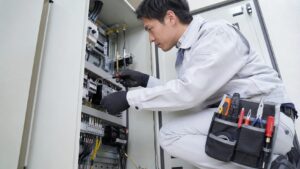 電気パネル作業をする日本人技術者と電工用工具ポーチ、ポケット配置を重視した収納例