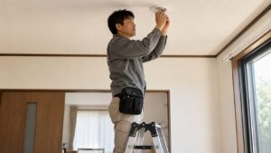 脚立で天井作業をする日本人男性と安全な工具ポーチ、落下防止を意識した作業風景