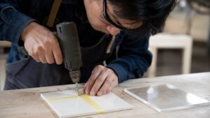 マスキングテープを貼ったタイルに慎重に穴あけする日本人作業者
