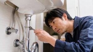 シンク下の配管ナットをモンキーレンチで調整する日本人男性