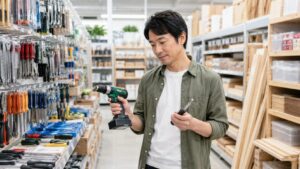ホームセンターの工具売り場で電動ドリルと手工具を比較する日本人男性
