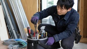 工具バケツにドライバーやペンチを立てて収納し、電工作業の準備をする日本人男性