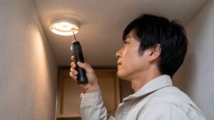 狭い場所で小型の7.2V電動ドライバーを使い照明器具を取り付ける日本人男性