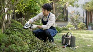 日本人男性が庭で充電式園芸工具を使って生垣を剪定している様子