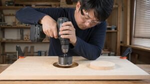 日本人作業者がホルソーで木材に大きな穴をあける様子