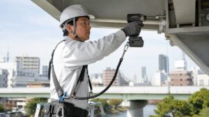 工具落下防止ストラップを付けたインパクトドライバーで高所作業をする日本人作業員