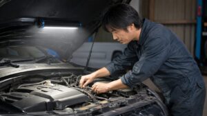 マグネット式LED作業ライトで車のエンジンルームを照らして整備する日本人男性