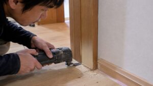 マルチツールで木製ドア枠の下端を面一切断する日本人男性