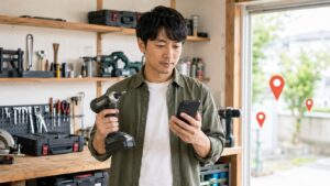 近くの工具買取店をスマートフォンで探す日本人男性と電動工具