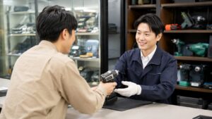 工具買取店で中古の電動工具を査定に出す日本人男性とスタッフ