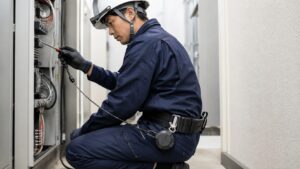 工具落下防止リールを腰に装着して電気設備を点検する日本人作業員
