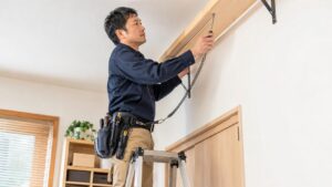工具落下防止ストラップを付けたドライバーで脚立作業をする日本人男性
