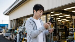 ホームセンター前でスマホを使って工具の在庫や営業時間を確認する日本人男性